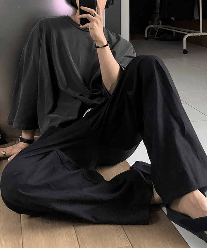 ダークグレーのオーバーサイズTシャツにブラックのワイドイージーパンツ、サンダルを合わせた人物の座っている写真。