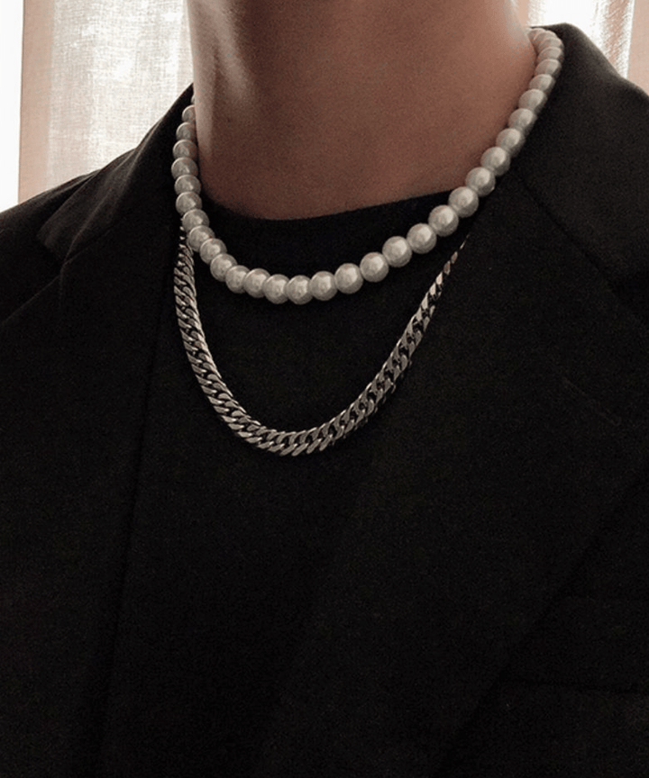 ニュアンスのある背景の前で、黒ジャケットの襟元から覗くレイヤードネックレス。