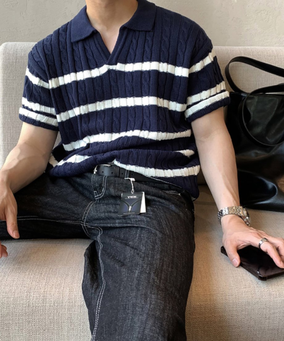 室内のソファに座り、ネイビーのスキッパー風ボーダーニットポロシャツをラフに着こなす男性の正面クローズアップ。