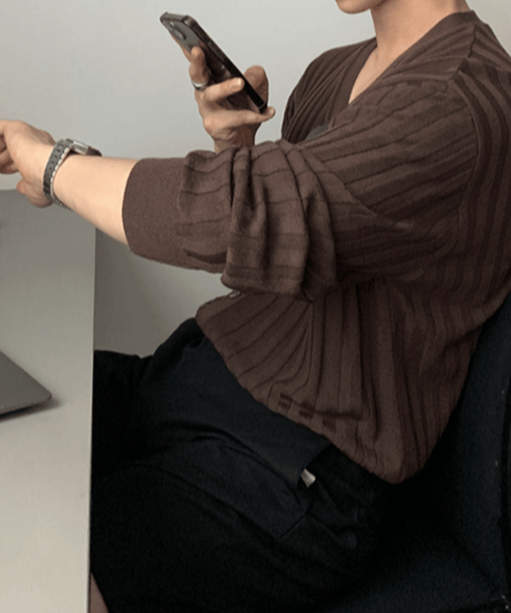 グレーのデスクに置かれたノートPCの前で、椅子に座りながらスマートフォンを操作し、左腕の腕時計を確認するような仕草を見せる男性のサイドカット。