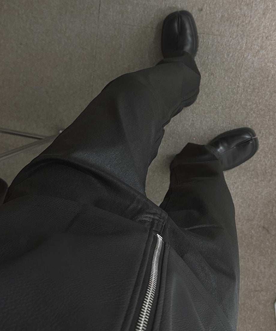 黒のフェイクレザージャケットと黒のスリムパンツ、つま先が分かれた黒のタビシューズを合わせた男性の足元を見下ろしたアングル写真。
