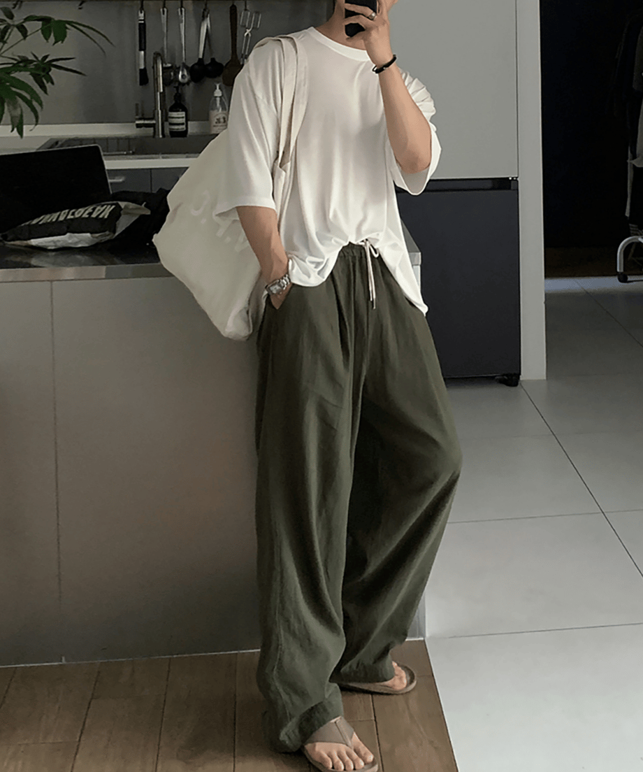 ホワイトのオーバーサイズTシャツにミリタリーグリーンのワイドパンツを合わせ、大きめの白トートバッグを肩に掛けた人物のスタイリングカット。