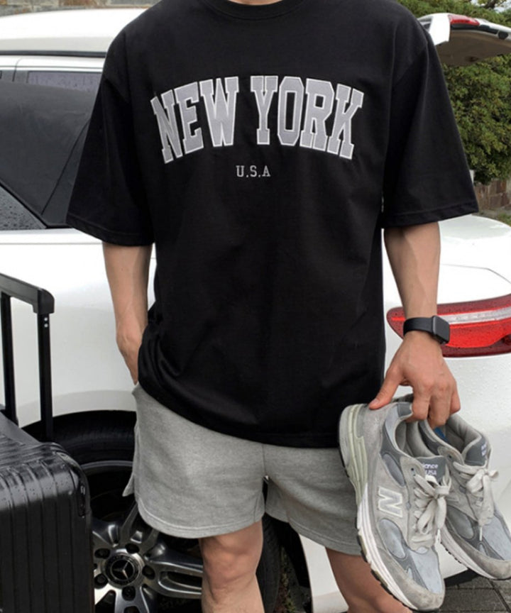 ブラックのNEW YORKロゴTシャツを着用し、手にグレーのスニーカーを持った男性のアップカット