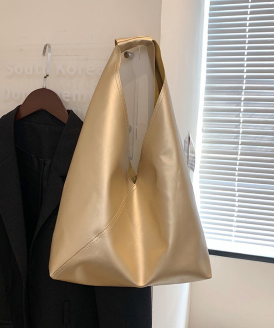 黒いジャケットが掛かったハンガーの隣にディスプレイされた、華やかで品のあるメタリックゴールドのトライアングルバッグ。