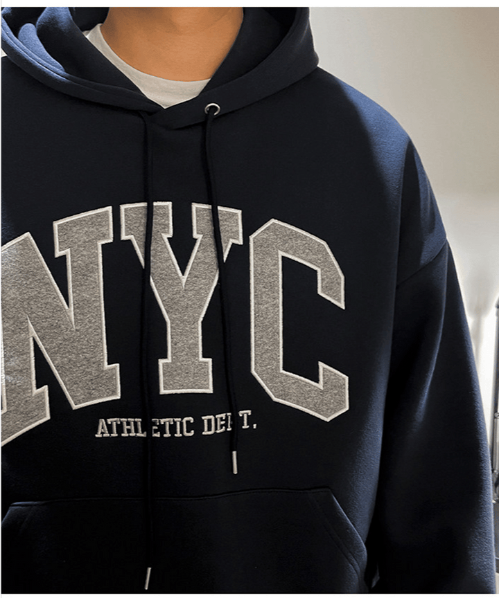 立体感のあるフードの立ち上がりと、フロントの「NYC ATHLETIC DEPT.」の緻密な刺繍・ワッペンディテールを強調したネイビーブルーのパーカーの拡大カット。