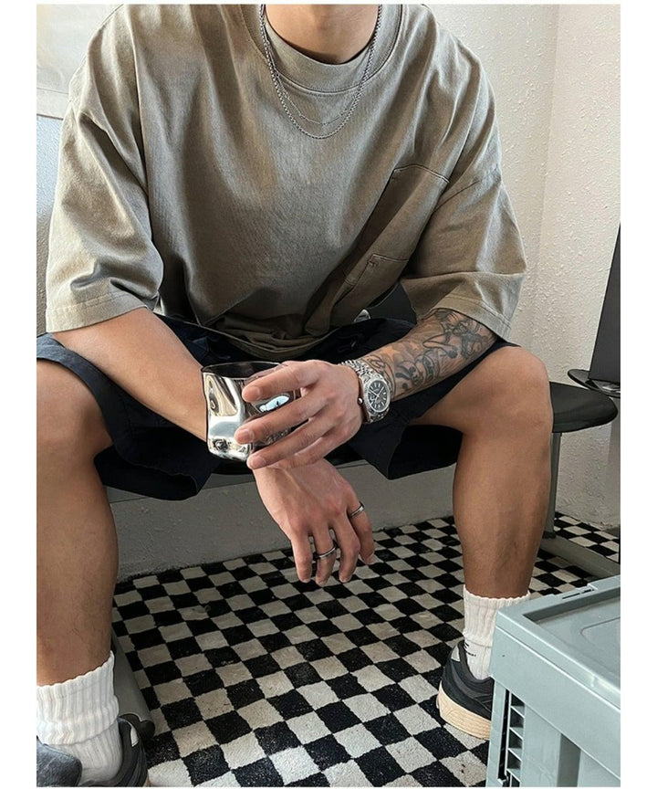 チェッカーフラッグ柄の絨毯が敷かれた部屋の椅子に腰掛け、ショーツとボリュームスニーカーを合わせた大人のストリートカジュアルな全身コーディネートカット。