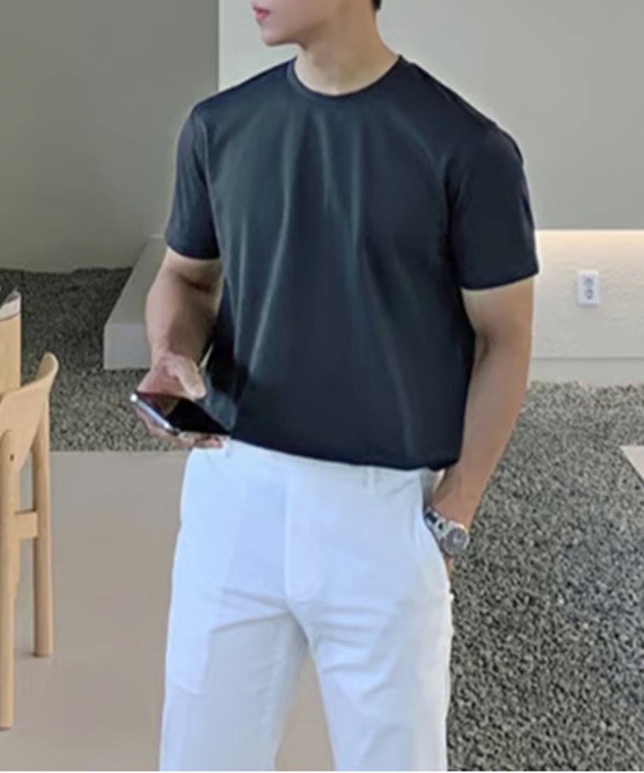 パープルのクルーネックTシャツにホワイトのスラックス、腕時計を合わせて室内に立つ男性の正面。