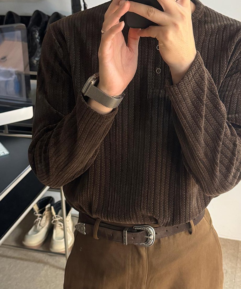 ブラウンのリブ編みヘンリーネックカットソーを着用した男性が、両手でスマートフォンを持ち、画面を見つめている胸元の写真。