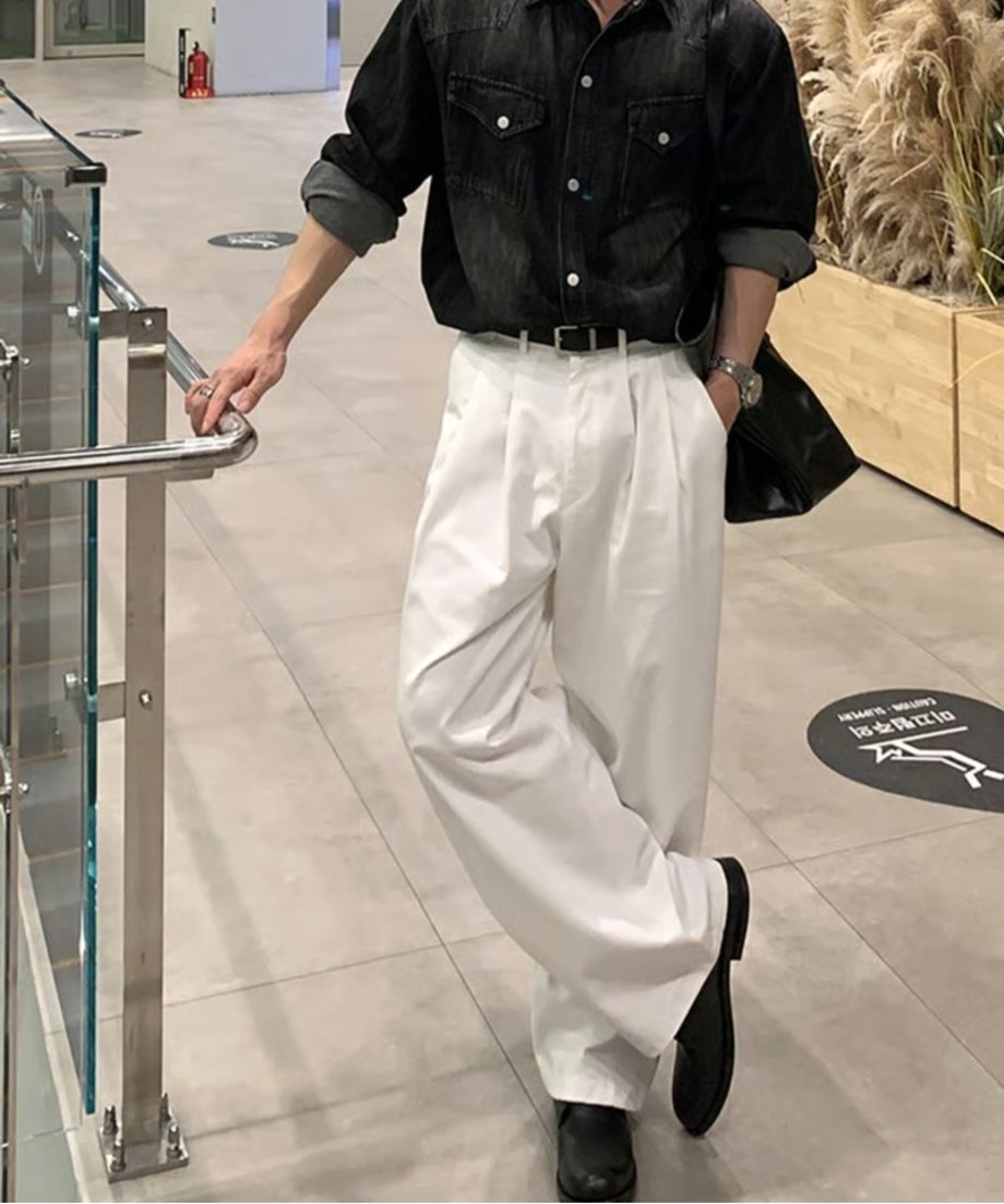 手すりのある通路で、黒のデニムシャツとホワイトのツータックワイドスラックス、黒のレザーシューズを着用して立つ男性の正面カット。