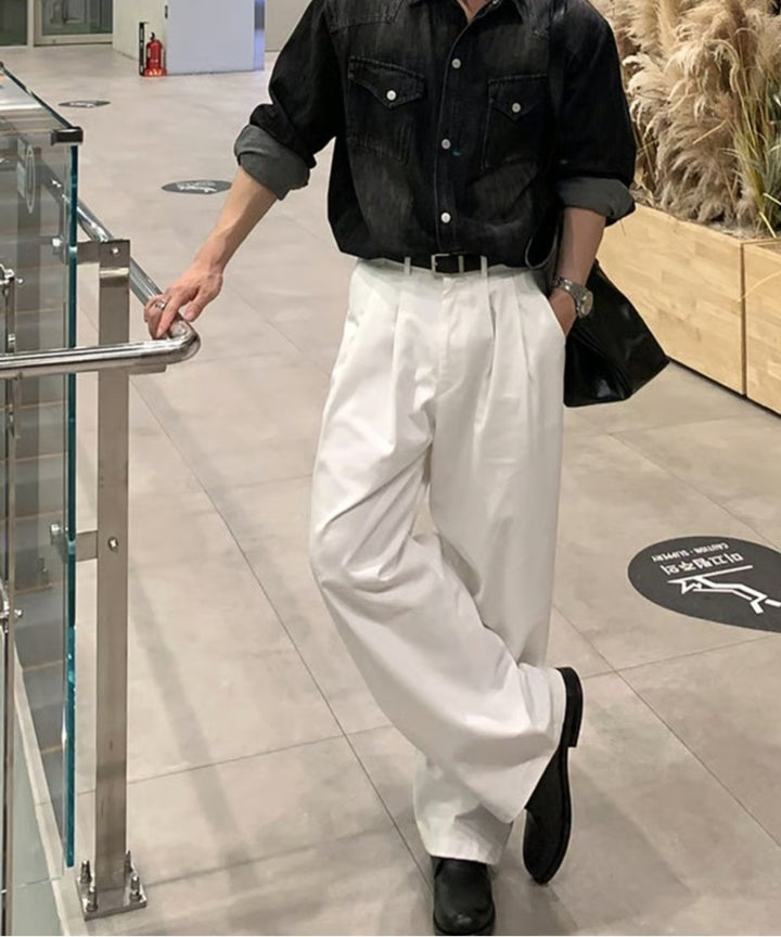 手すりのある通路で、黒のデニムシャツとホワイトのツータックワイドスラックス、黒のレザーシューズを着用して立つ男性の正面カット。