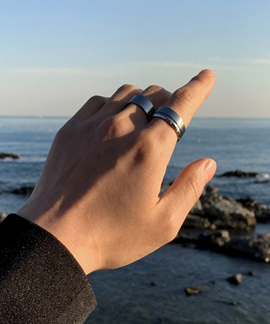 広大な海と岩場を背景に、リングを着用した手を優しく掲げる男性のカット。