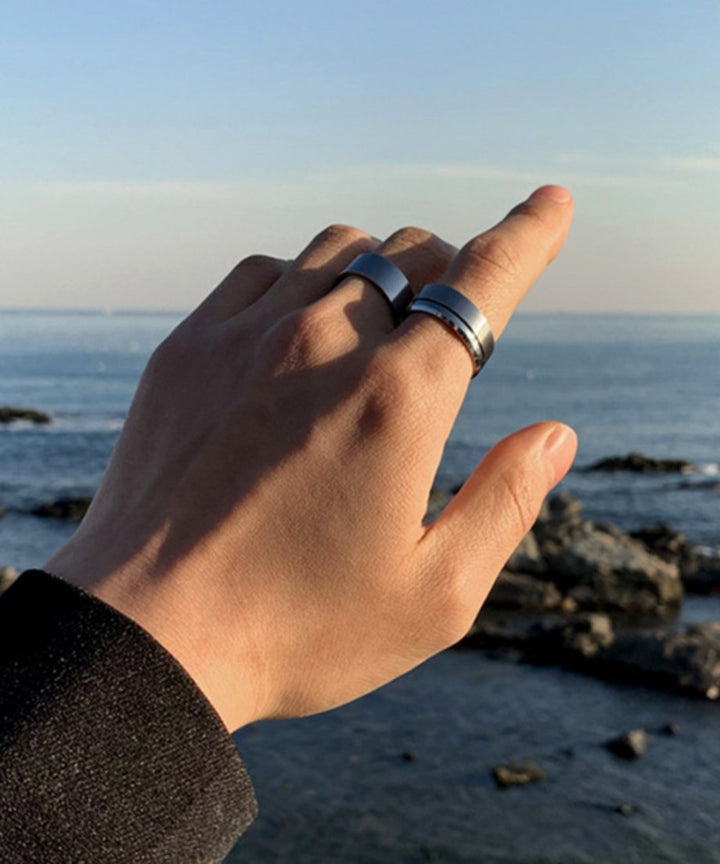 広大な海と岩場を背景に、リングを着用した手を優しく掲げる男性のカット。