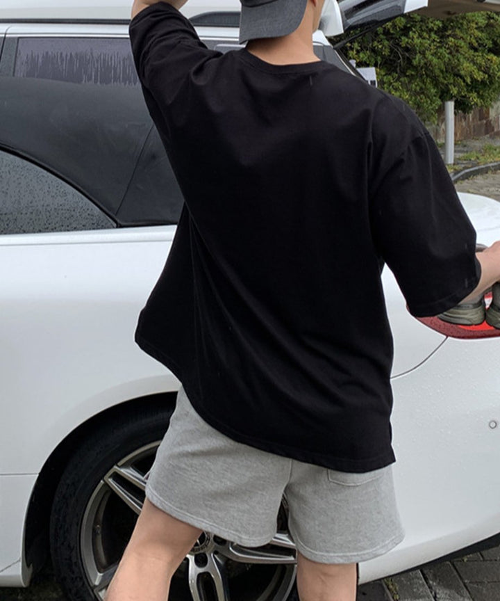ブラックのロゴTシャツにグレーのショーツ、グレーのキャップを後ろ被りにした男性の後ろ姿