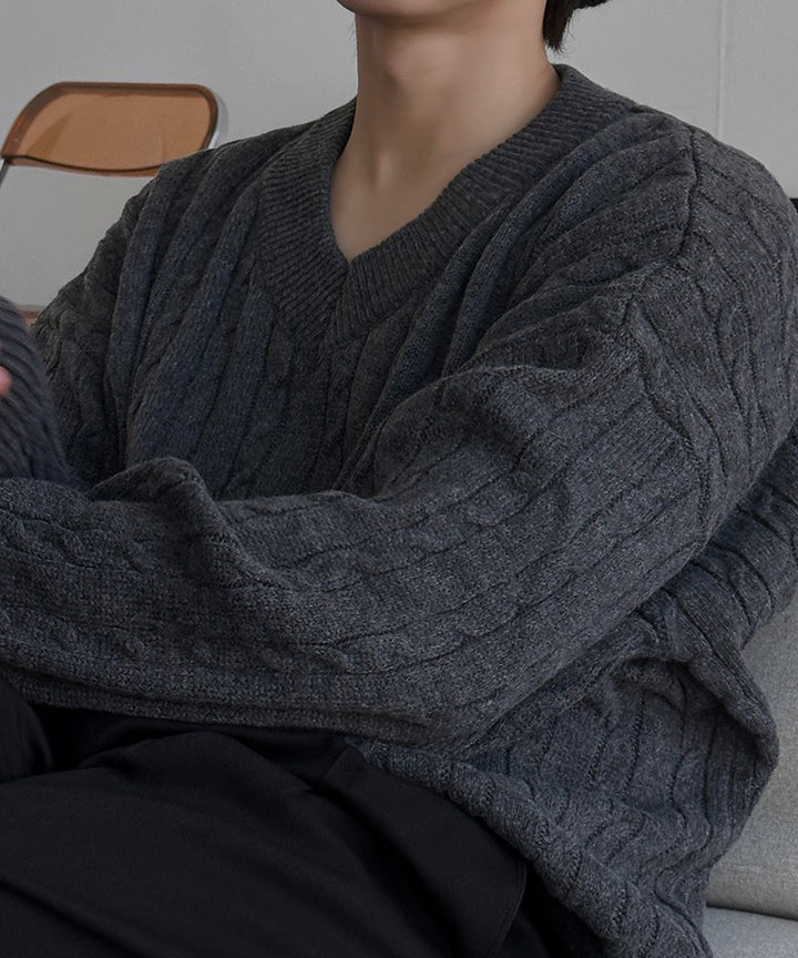ネックの開き具合と立体的なケーブル編みの質感が伝わる、ダークグレーニットを着用した男性のバストアップカット。