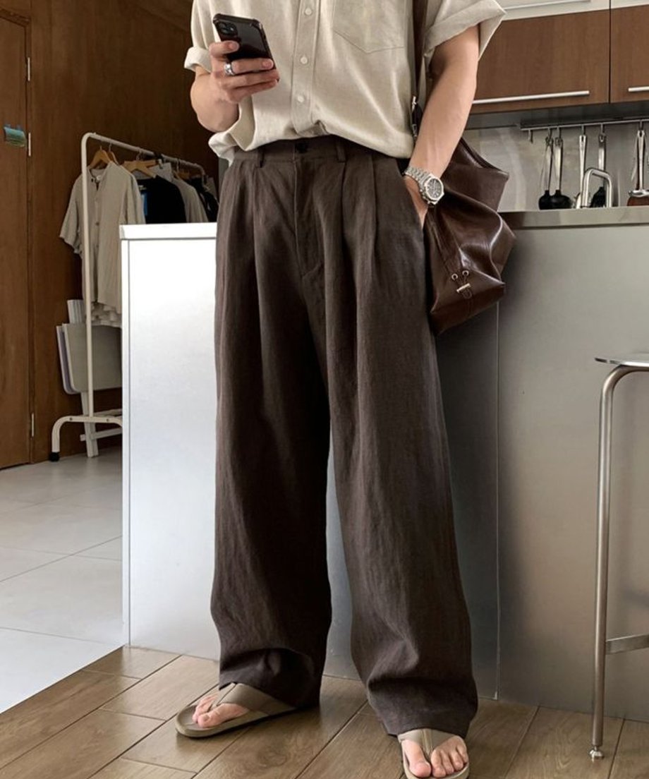 フラワーベージュの半袖シャツにコーヒー色のツータックワイドパンツを合わせ、茶色のレザーバッグを持った男性の正面。