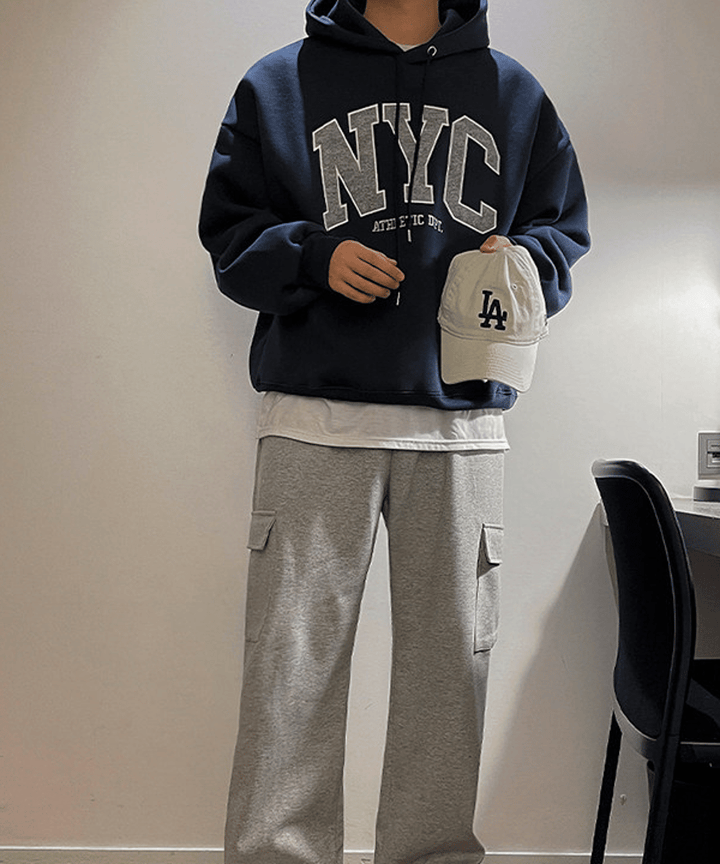 ネイビーブルーのNYCビッグロゴパーカーに、白Tシャツをレイヤードし、グレーのカーゴスウェットパンツを合わせたメンズストリートスタイル。
