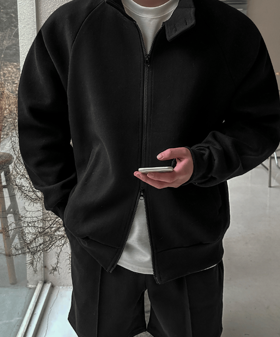 黒のジップアップジャケットを着用し、インナーの白Tシャツを見せながら手元でスマートフォンを操作する男性のアップ