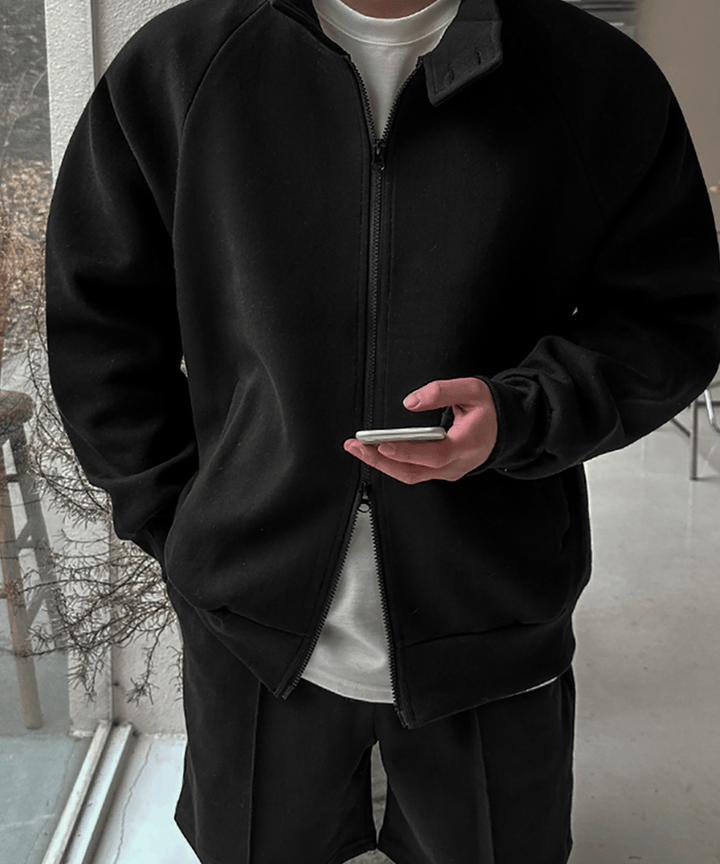 黒のジップアップジャケットを着用し、インナーの白Tシャツを見せながら手元でスマートフォンを操作する男性のアップ