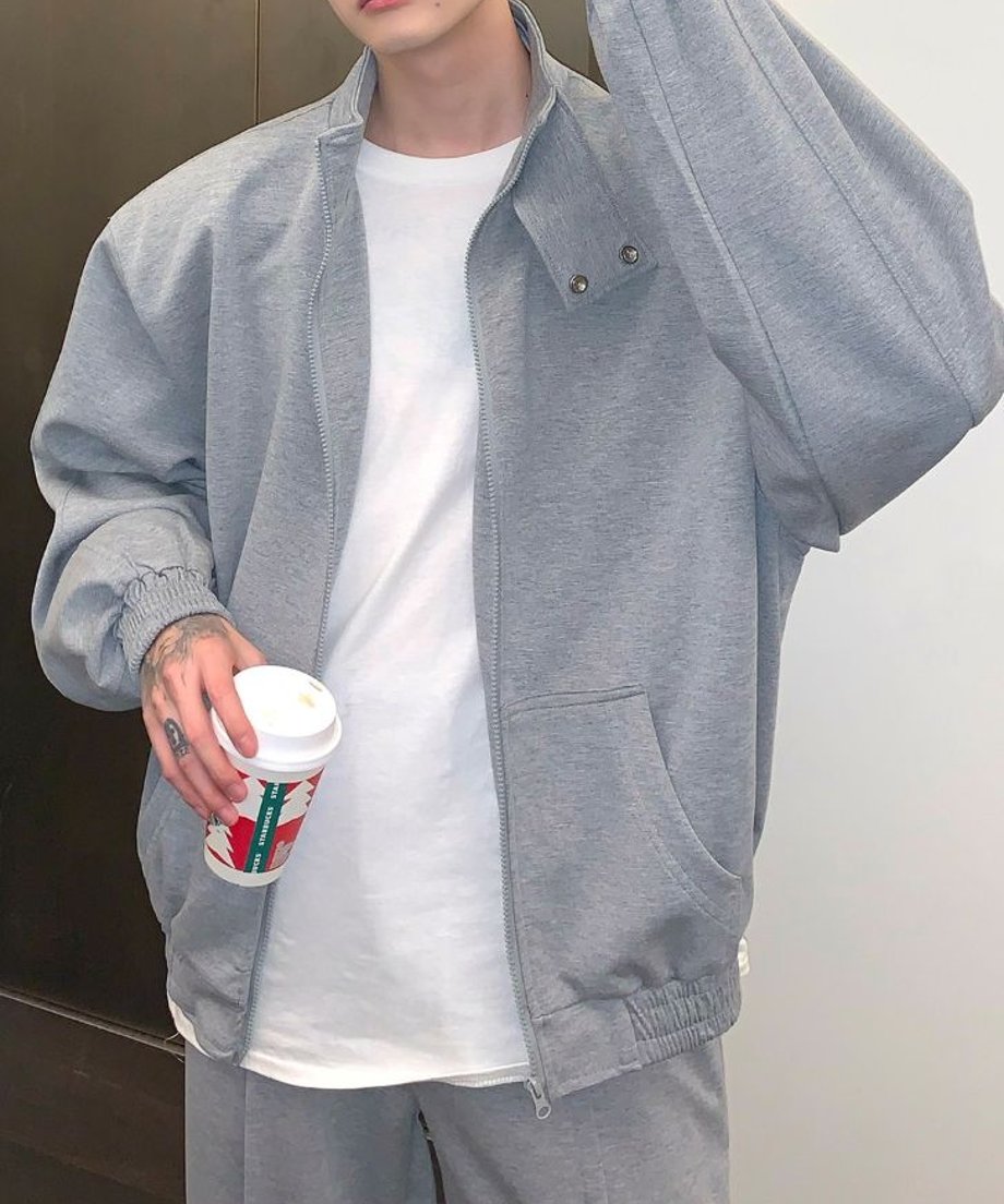 グレーのブルゾンを着た男性の、フロントのカンガルーポケットや全体のゆったりとしたビッグシルエットが際立つ斜め正面からの上半身カット。