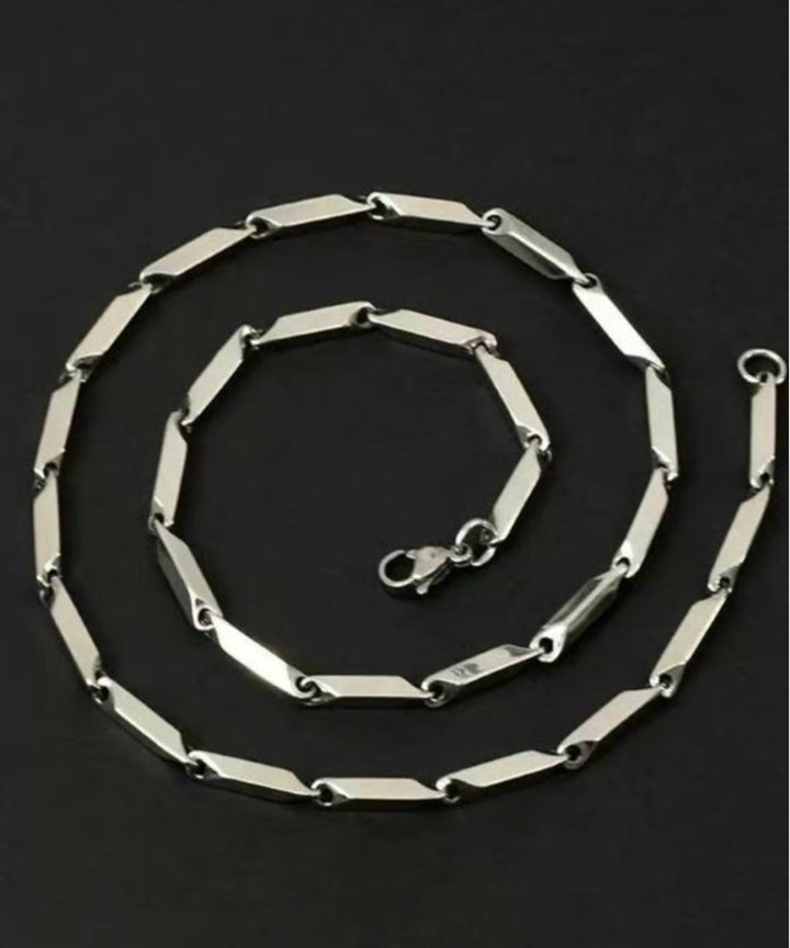 フラットな黒背景の上で、カニカン留め具を中心に2重の綺麗な円を描くように丸められた、洗練されたデザインチェーンの俯瞰置き画カット。
