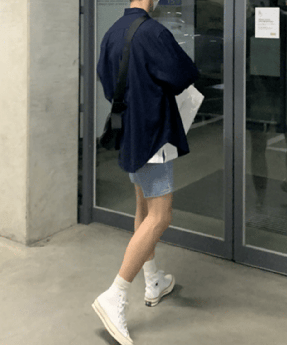 ネイビーの長袖シャツを着用し、白いハイカットスニーカーに白いソックスを合わせて施設に入る男性の斜め後ろからの全身カット。