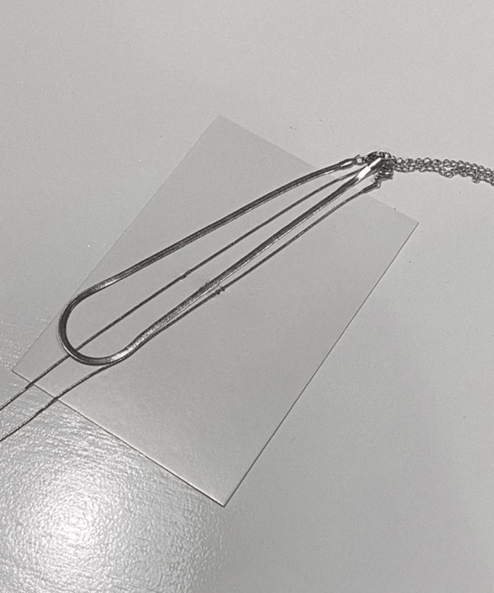 白いカードの上にU字型に美しく並べられた、2本の異なるチェーンの長さの対比と、すっきりとした全体のシルエットが分かりやすいフラットレイカット。