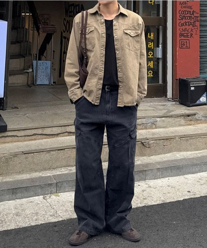 黒のインナーにカーキブラウンのシャツを羽織った人物が、ブラックのワイドカーゴバギーパンツを穿いて道路際に立っている全身スタイリング写真。