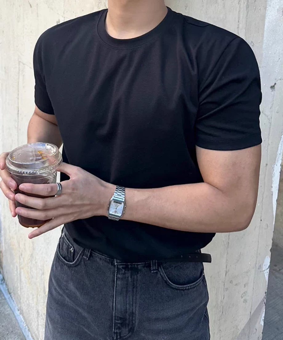 黒い半袖クルーネックTシャツを着用し、両手でドリンクのカップを持って立つ男性の正面近くからのクローズアップショット。