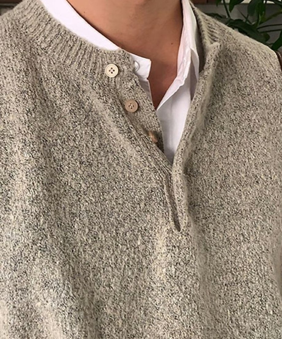 ベージュのヘンリーネックニットのネックラインに並ぶ丸いボタンと、インナーの白シャツのレイヤードを強調したクローズアップカット。