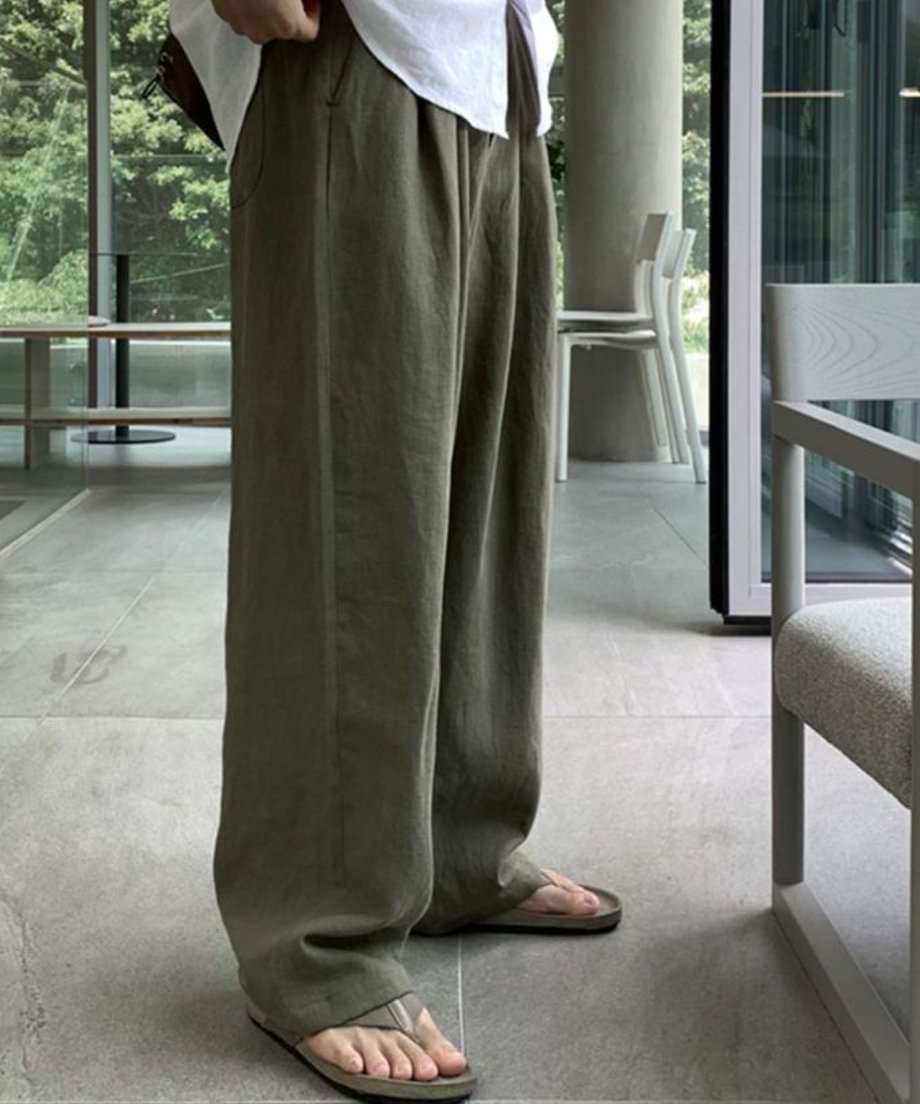 アーミーグリーンのツータックワイドパンツとトングサンダルを着用した男性の横からのシルエット。