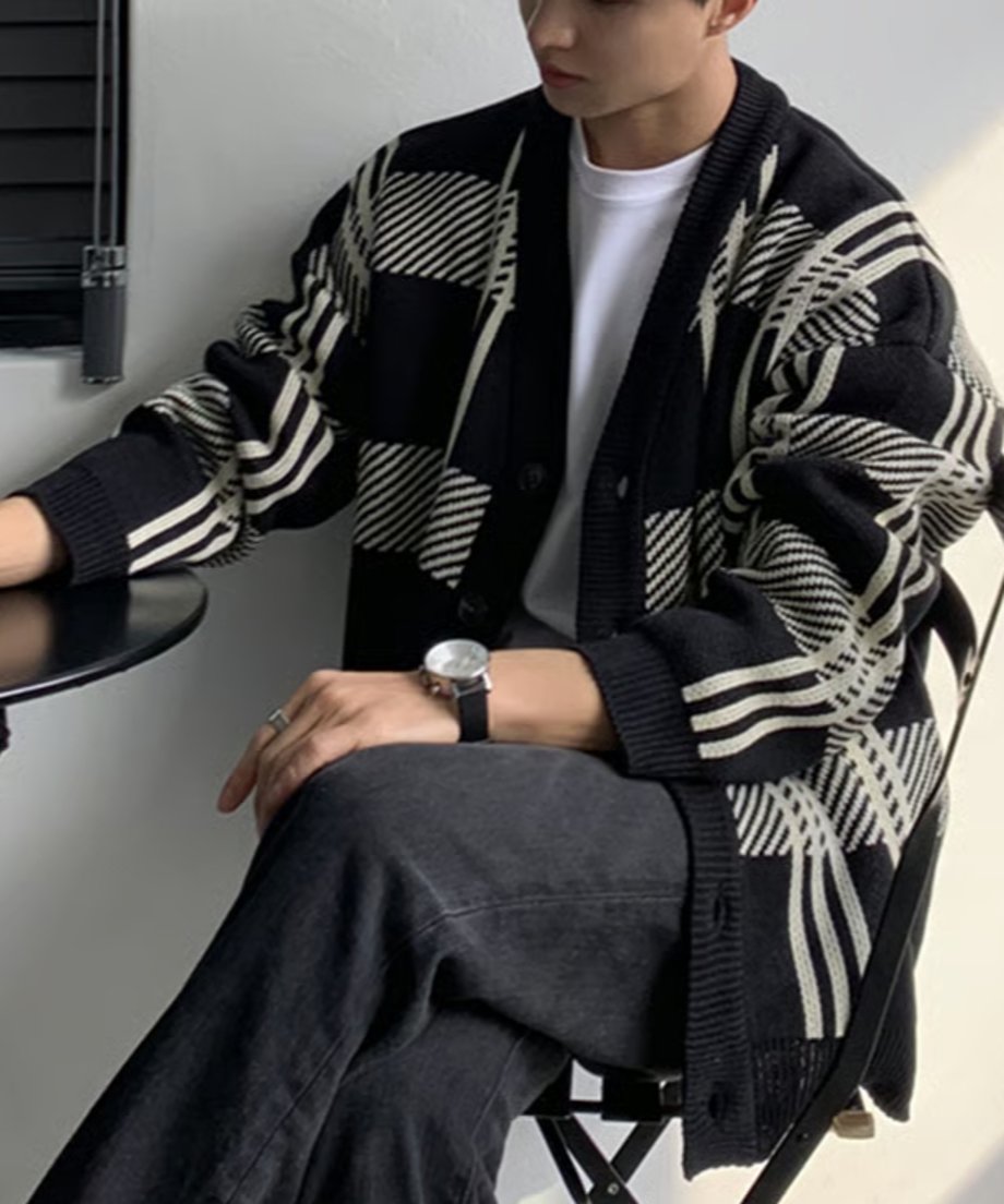 ブラックチェックのカーディガンを着用した男性が、カフェの黒いアイアンチェアに座っているサイドフロントのアップカット。