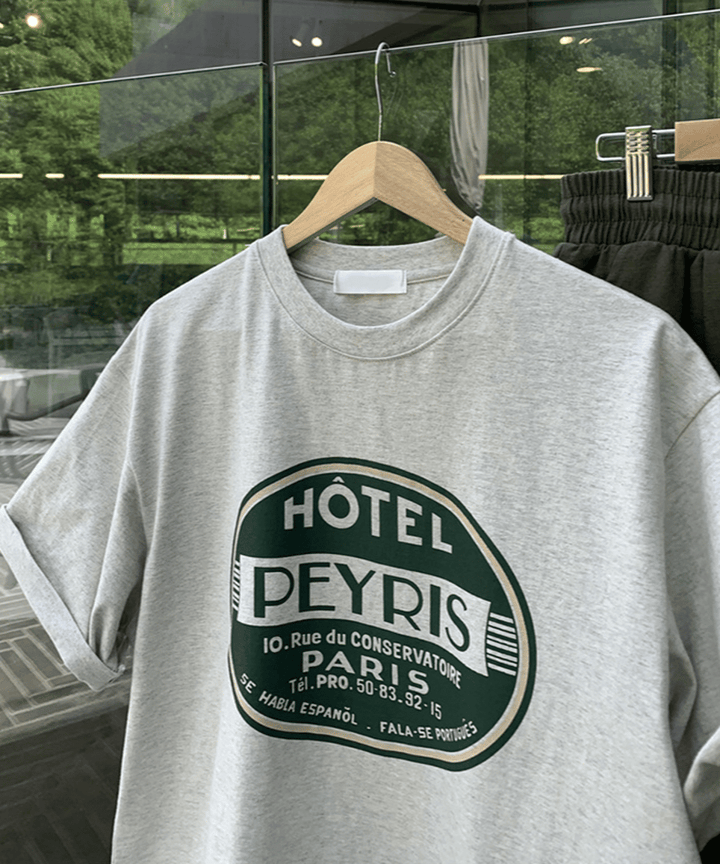 ハンガーに掛けられたメランジグレーのレトロホテル風サークルロゴTシャツのディテールカット。