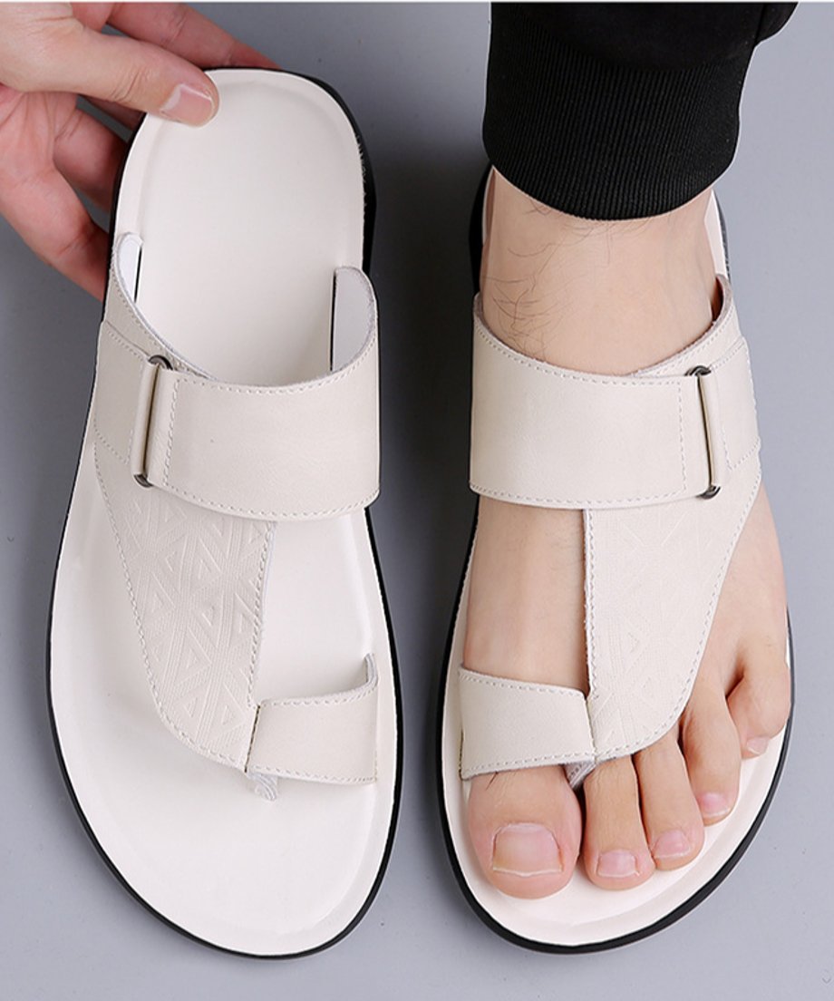 グレーの背景で、黒い裾絞りのパンツを穿いた男性がホワイトのトングサンダルを着用している足元の真上からのカット。