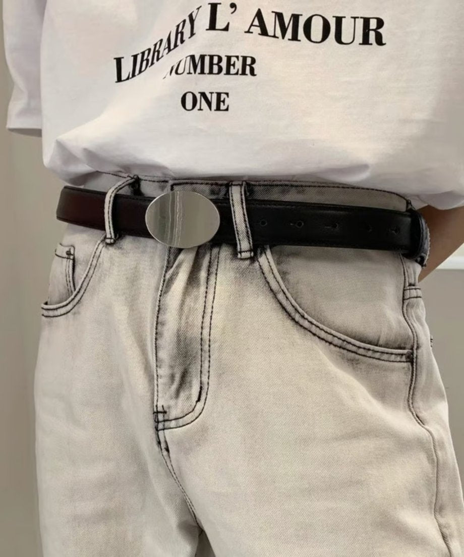 フロントにロゴがプリントされた白いTシャツをウォッシュ加工のグレーデニムにインし、ウエストマークとしてシルバーオーバルバックルの黒ベルトを合わせたストリート調のスタイリングカット