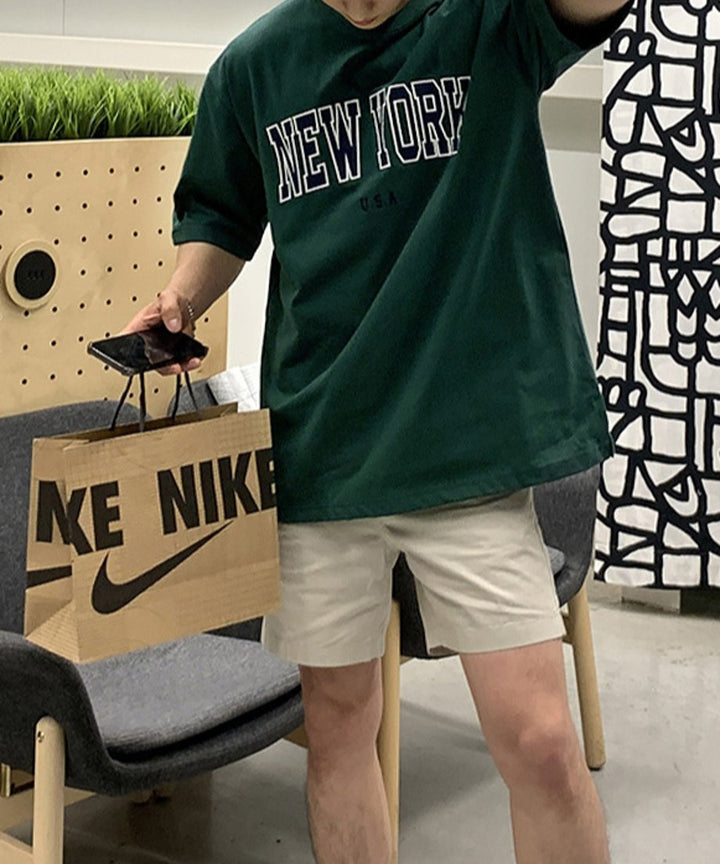 ダークグリーンのNEW YORKロゴTシャツにベージュのハーフパンツを合わせた男性の正面からのコーディネート
