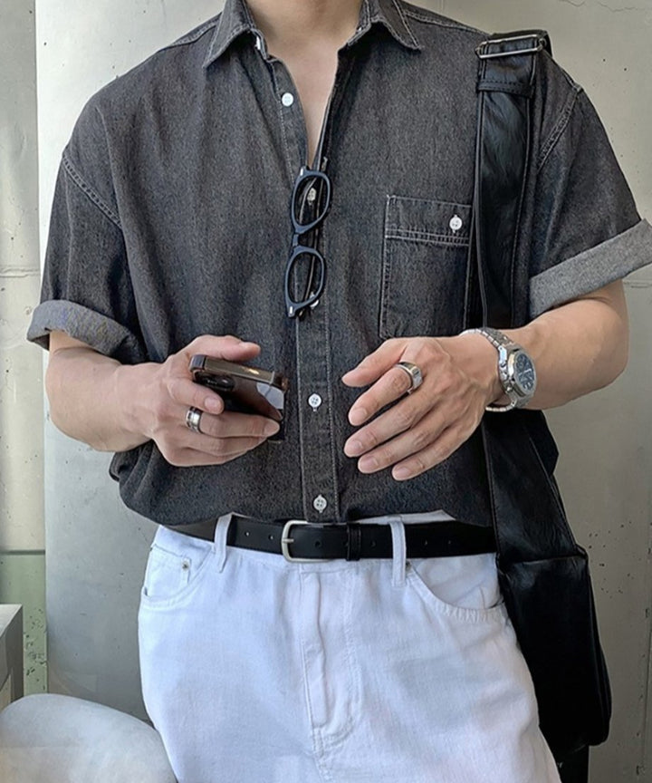 ブラックデニムの半袖シャツにホワイトのパンツ、黒いレザーのショルダーバッグを合わせ、両手にスマートフォンを持つ男性の手元とチェストアップ。