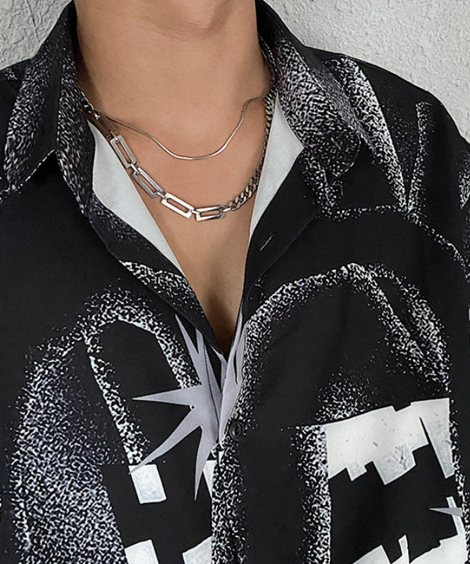 総柄シャツの襟元から覗く、2種類の異なるチェーンがドッキングされた洗練されたメタルネックレスのクローズアップ