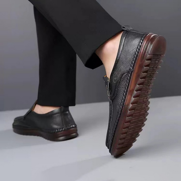 ブラックのカジュアルローファーを穿いて歩く男性の、波型のアウトソール裏が見える後ろ姿の足元写真