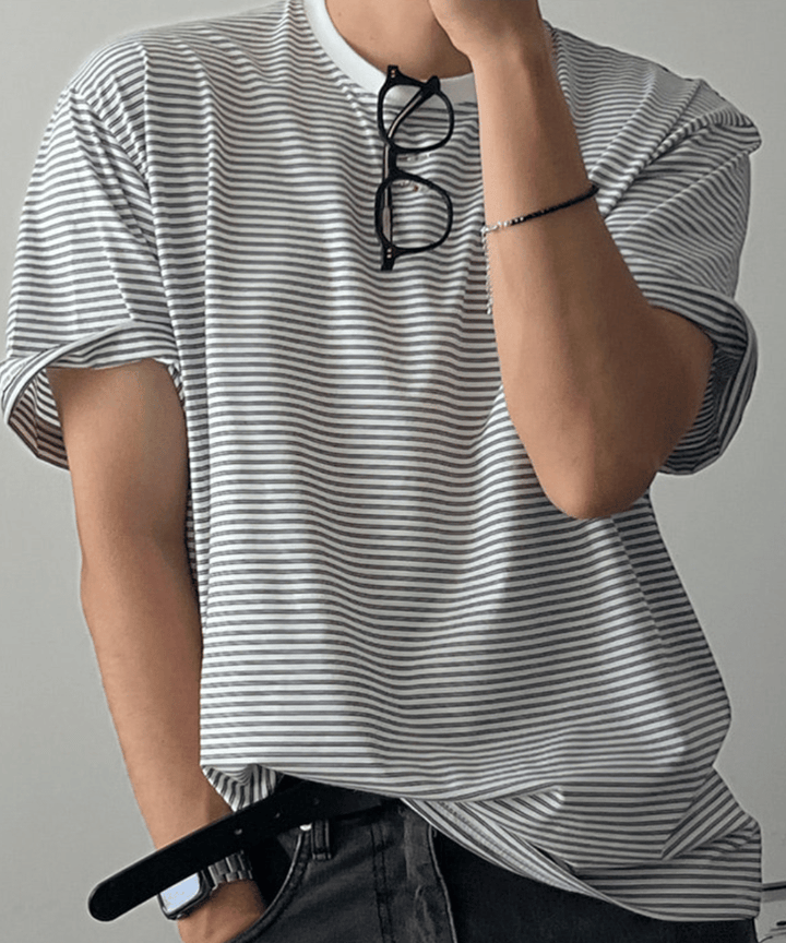 グレーのマルチストライプ柄のTシャツを着た男性。片手をポケットに入れて首にはサングラスを掛けている。