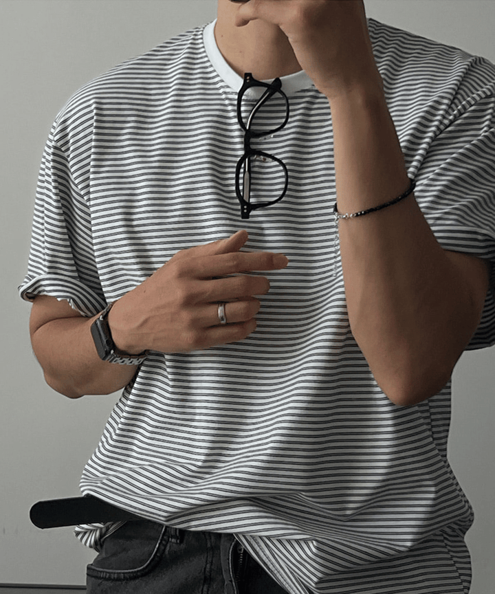 グレーのマルチストライプ柄のTシャツを着た男性が首にサングラスを掛けた半身ショット。