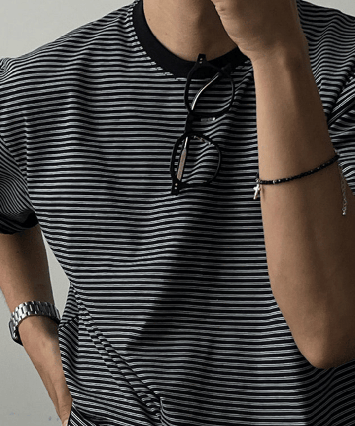 ブラックのマルチストライプ柄のTシャツを着た男性のバストアップショット。首にサングラスを掛けています。