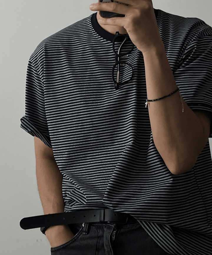 ブラックのマルチストライプ柄Tシャツを着用した男性のバストアップ。落ち着いたトーンの配色が特徴です。