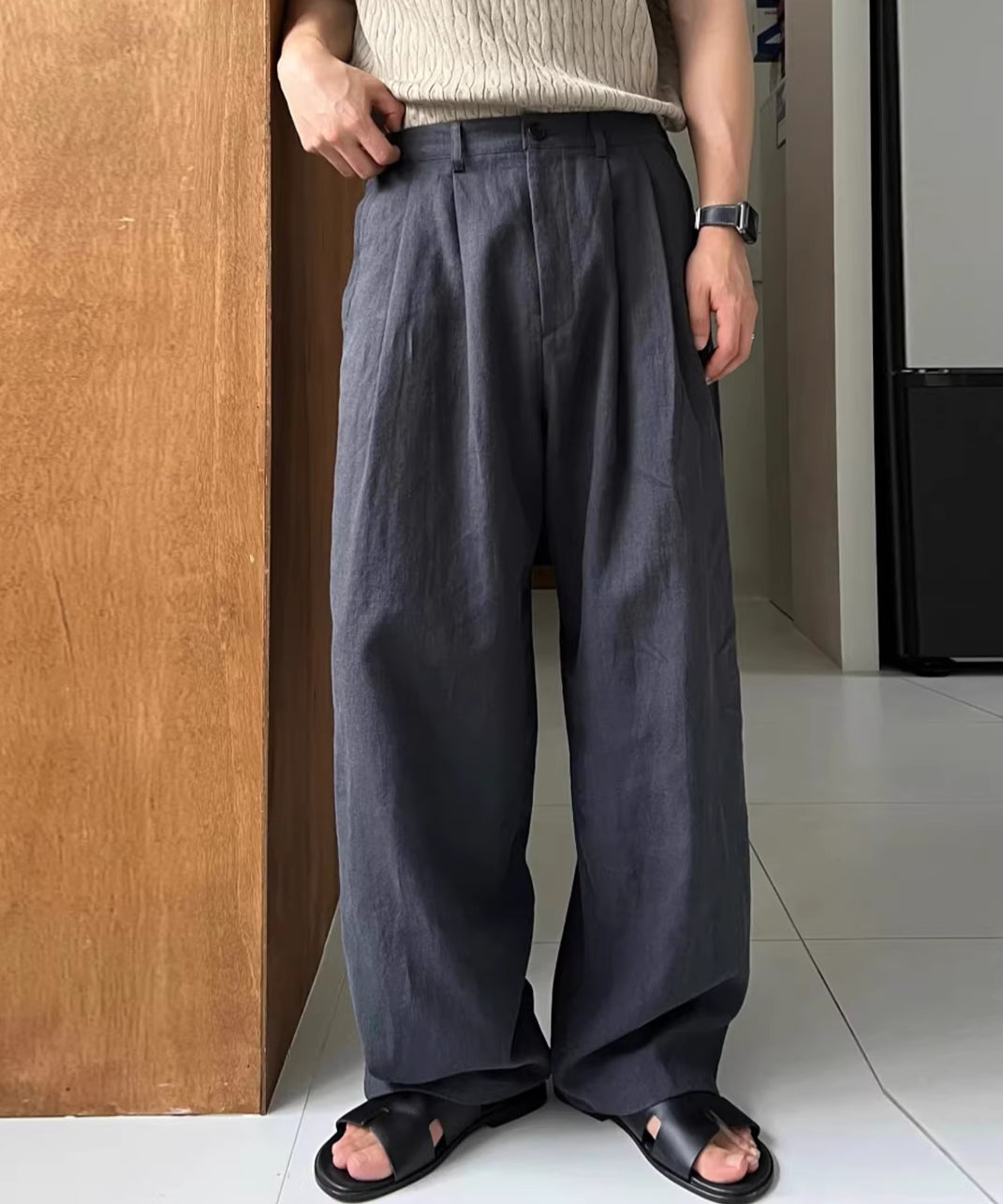 ネイビーのプリーツワイドパンツに黒のレザーサンダルを合わせた男性の足元の写真