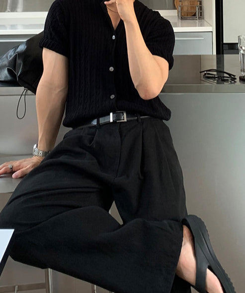 ブラックのプリーツワイドパンツに黒の半袖シャツ、黒のトングサンダルを合わせたワントーンコーデで腰掛ける男性
