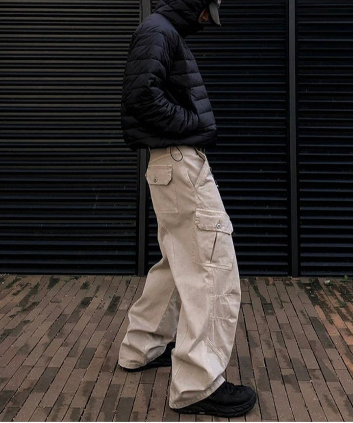 黒のダウンジャケットにカーキのワイドバギーカーゴパンツ、黒スニーカーを合わせた男性の、屋外でのクールな横向きの立ち姿。