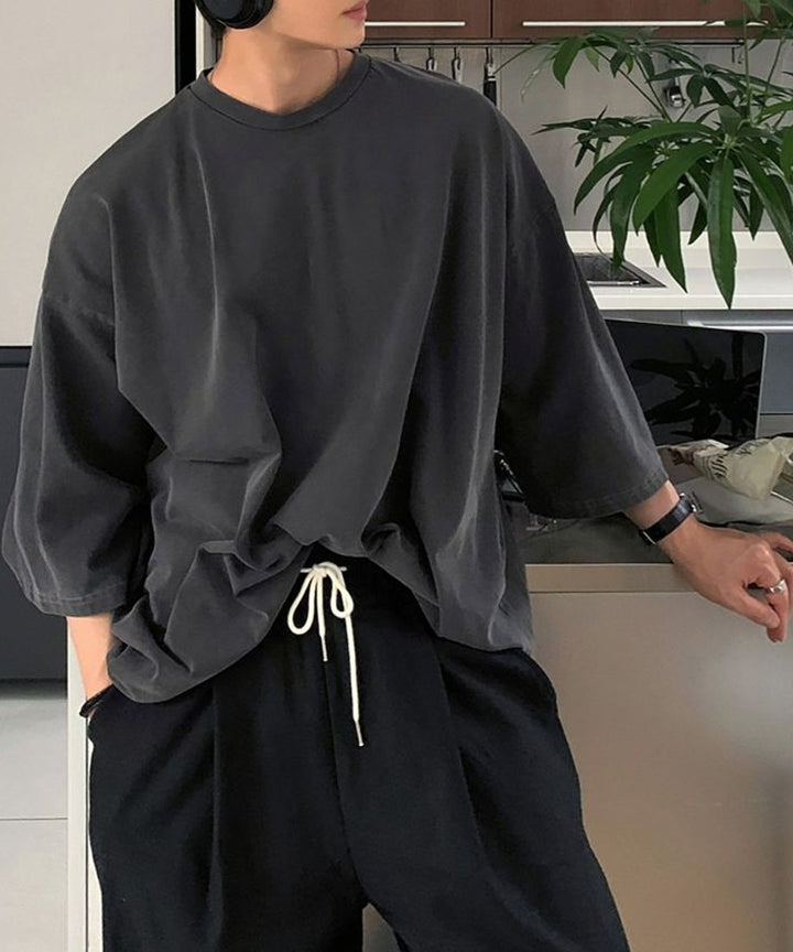 アイアングレーのオーバーサイズTシャツに、白いドローコードがついた黒のイージーパンツを合わせた男性の上半身ショット。