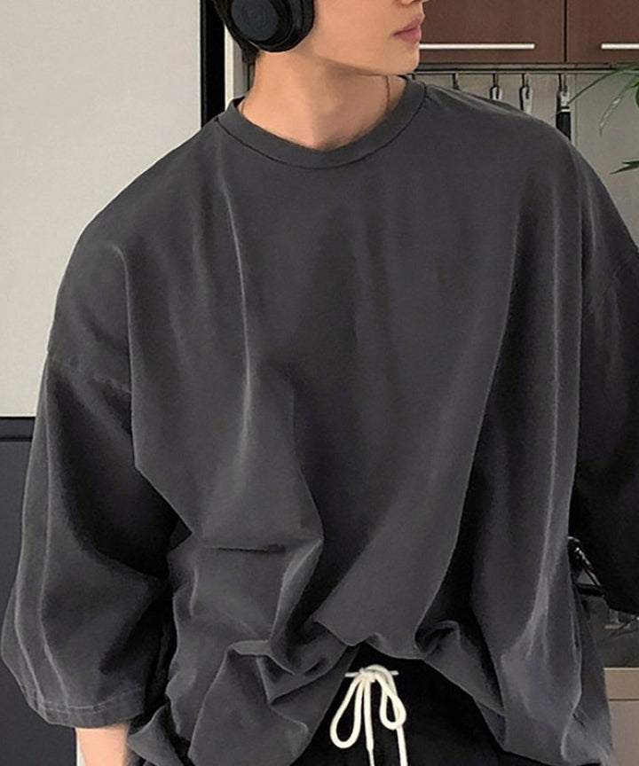 アイアングレーのオーバーサイズTシャツに、白いドローコードがついた黒のイージーパンツを合わせ、ヘッドホンを首にかけた男性の上半身スタイル。