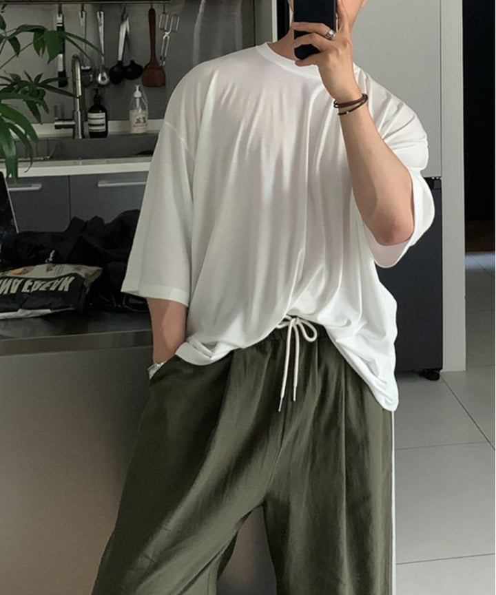 鏡越しに自撮りをする、ホワイトのビッグTシャツをルーズにタックインし、カーキのイージースラックスを合わせた男性のフロントカット。