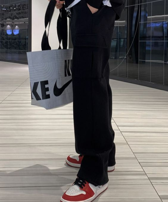 ブラックのスウェットカーゴパンツに赤と白のスニーカーを合わせ、左手にのトートバッグを提げて立つ男性のサイドスタイリング。
