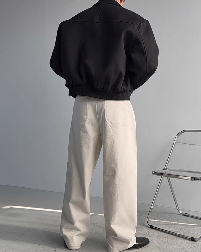 ブラックのスタンドカラーブルゾンに白のワイドパンツ、黒の革靴を合わせた男性の全身後ろ姿。